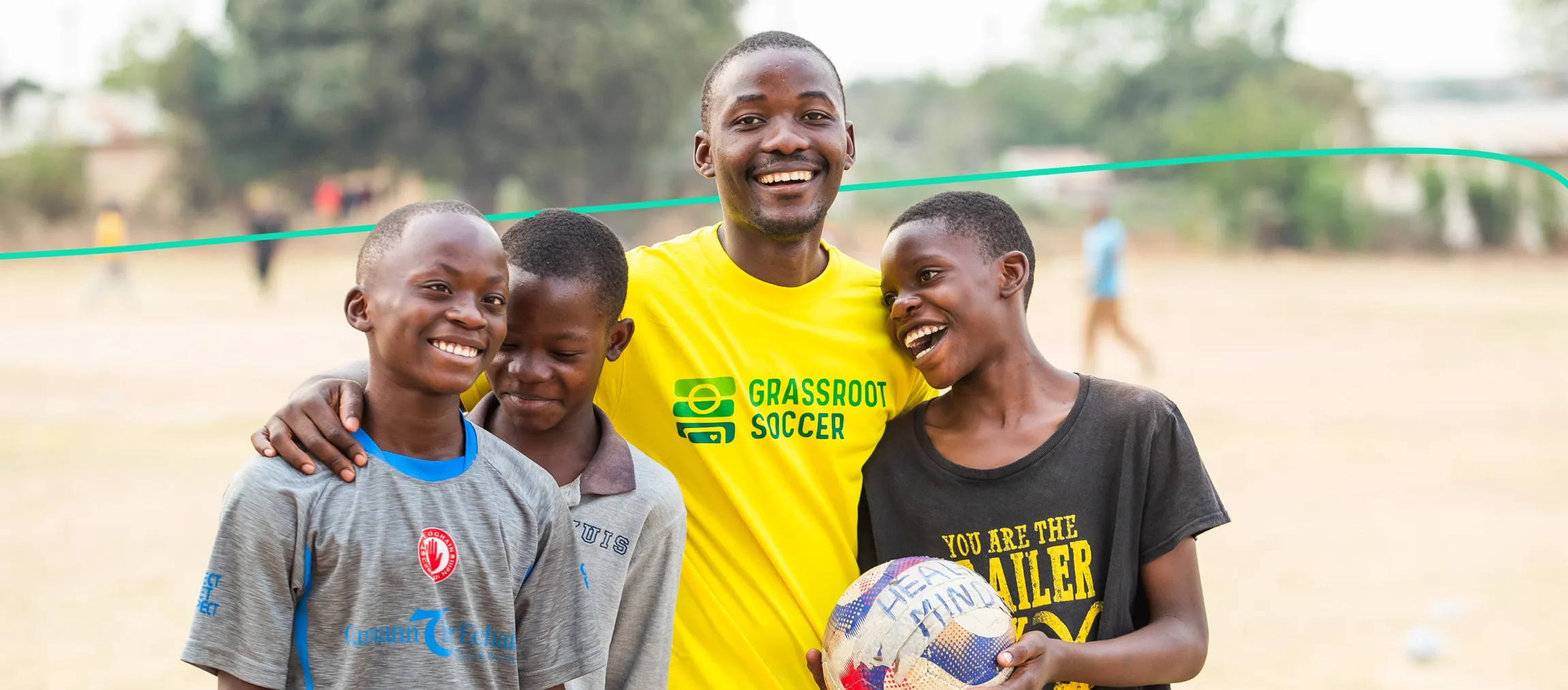 A Grassroot Soccer coach smiling with three young players on a soccer field.